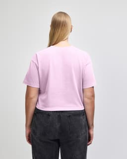 A back view of a pink cropped boxy t-shirt made from heavyweight cotton, worn with blue jeans. Features a logo.