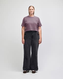 A heavyweight cotton women's crop boxy t-shirt in a muted purple, paired with blue jeans. The model stands against a plain background.
