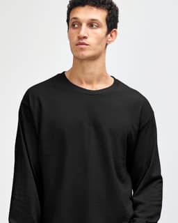 A heavyweight cotton unisex long sleeve t-shirt in black, featuring a logo, displayed on a model.