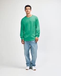 A unisex long sleeve t-shirt in a light aqua colour, paired with loose-fit blue jeans and black sneakers.