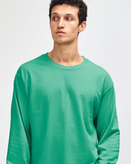 A turquoise heavyweight cotton unisex long sleeve T-shirt on a model, featuring a logo on the sleeve.
