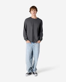 A heavyweight unisex long sleeve t-shirt in grey, paired with light blue jeans and black sneakers, displayed on a model.