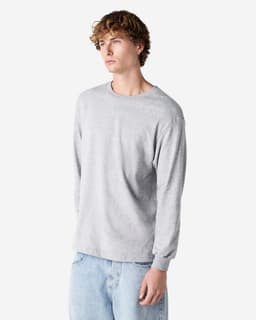 A grey heavyweight cotton unisex long sleeve T-shirt with a casual fit. The model is standing in a relaxed pose.