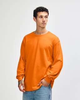 An orange heavyweight cotton unisex long sleeve t-shirt displayed on a model, featuring a simple design and sleeves with cuffed ends.