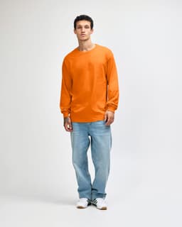 An orange heavyweight cotton unisex long sleeve t-shirt paired with blue jeans, worn by a model.