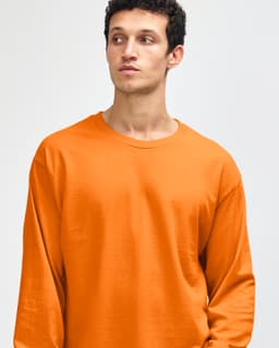 An orange heavyweight cotton unisex long sleeve t-shirt displayed on a model. The shirt has a simple design and logo.