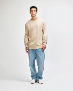 A lightweight long sleeve T-shirt in beige, paired with blue jeans, worn by a model in a casual pose.