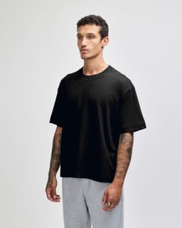 A black unisex boxy t-shirt made of heavyweight cotton, displayed on a model with tattoos, paired with light grey pants.