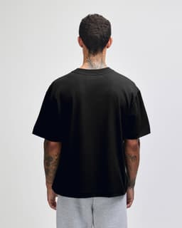 A black heavyweight cotton unisex boxy T-shirt displayed from the back, worn over grey shorts.