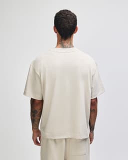 A boxy unisex t-shirt in a light beige colour, featuring short sleeves and a plain design, with a logo on the back.