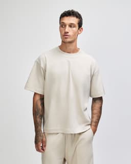 A unisex heavyweight cotton boxy t-shirt in a light beige colour, worn by a model with tattoos.
