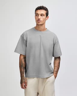 A grey heavyweight cotton unisex boxy t-shirt displayed on a model, featuring a relaxed fit and short sleeves.