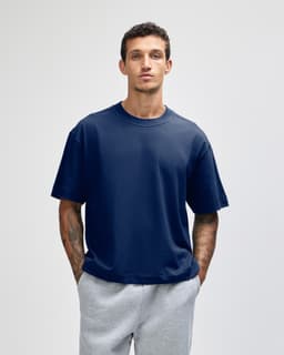 A navy unisex boxy T-shirt featured on a model, paired with grey sweatpants. The shirt has a branding logo.