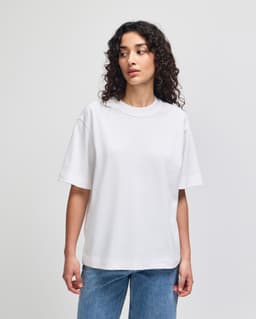 A white unisex boxy t-shirt made of heavyweight cotton, displayed on a model with curly hair.