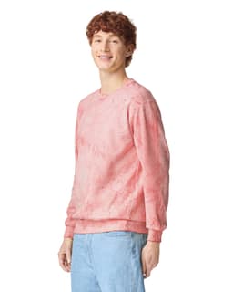 A pink crewneck sweatshirt displayed on a model, featuring a subtle tie-dye effect and a logo on the sleeve.