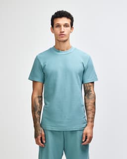 A unisex mockneck t-shirt in a soft green hue, featuring short sleeves and a relaxed fit. It has a logo on it.