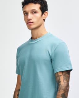 A teal unisex pique mockneck t-shirt with short sleeves, featuring a logo on the front.