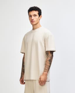 A unisex mockneck t-shirt in a neutral beige colour, displayed from the side, featuring a simple design and logo.