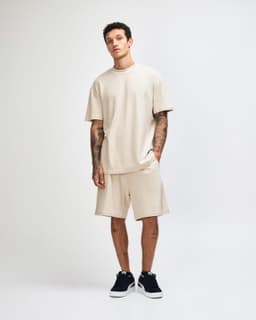 A model stands in a beige unisex mockneck T-shirt and matching shorts, paired with black footwear.