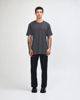 A unisex fine jersey short sleeve t-shirt in black, worn with beige pants and blue sneakers, with a logo visible.