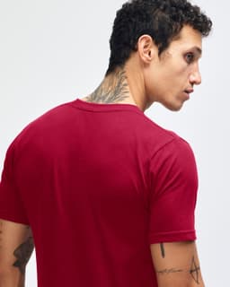 A maroon unisex fine jersey short sleeve t-shirt is displayed on a model wearing blue jeans. The shirt has a logo.