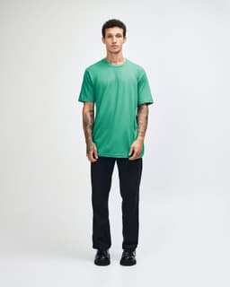 A model wearing a turquoise unisex fine jersey short sleeve t-shirt paired with khaki pants. The shirt has a logo.