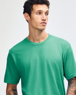 A green short sleeve t-shirt with a crew neck design, featuring a model with tattoos and curly hair.