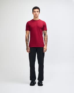 A maroon unisex fine jersey short sleeve t-shirt is displayed on a model standing casually with hands in pockets.