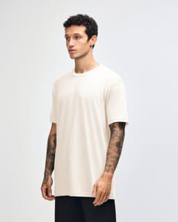 A side view of a beige unisex short sleeve t-shirt worn by a model, featuring a logo on the sleeve.