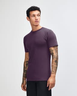 A purple unisex short sleeve t-shirt displayed from the side, featuring a simple design and a brand logo.