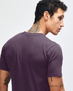 A model wearing a purple unisex short sleeve t-shirt paired with beige cargo pants and sneakers. The t-shirt has a logo.