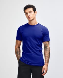 A blue unisex short sleeve t-shirt displayed on a model with curly hair. Features a logo on the shirt.