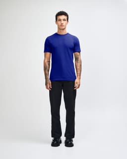 A unisex fine jersey short sleeve T-shirt in navy blue, worn by a model with curly hair, paired with beige pants.