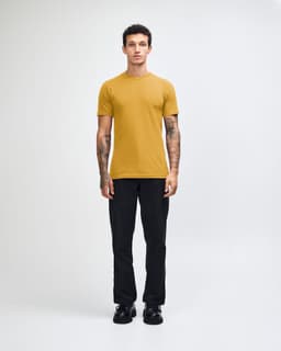 A model wearing a mustard yellow unisex short sleeve t-shirt paired with light blue baggy jeans and black shoes.