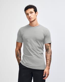 A grey unisex short sleeve T-shirt displayed on a model with hands in pockets, featuring a simple design.