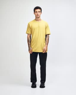 A model wearing a yellow unisex fine jersey short sleeve t-shirt and loose blue denim jeans, hands in pockets.