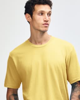A model wearing a yellow American Apparel Fine Jersey short sleeve t-shirt. The shirt features a logo.