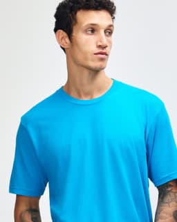 A unisex fine jersey short sleeve t-shirt in bright blue, paired with khaki pants. The model stands straight with a neutral expression.