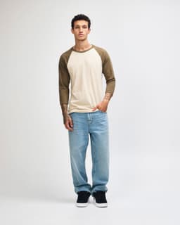 A unisex raglan T-shirt in cream with brown sleeves, paired with light blue cargo pants. Features a logo.