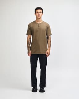 A unisex henley T-shirt in olive green, paired with light blue baggy jeans, displayed on a model.