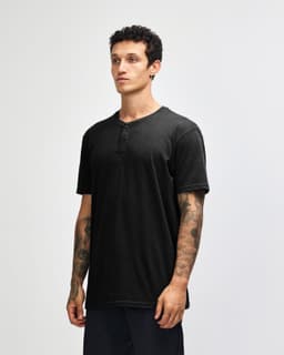 A black unisex Henley t-shirt with short sleeves and buttons, worn by a model with tattoos.