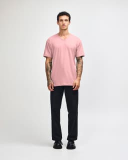 A unisex V-neck T-shirt in pink, worn by a model. The outfit includes black trousers and shoes.