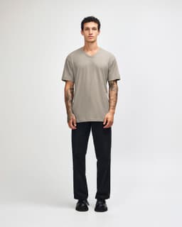 A unisex beige V-neck T-shirt displayed on a male model, paired with black pants. The shirt has a logo.