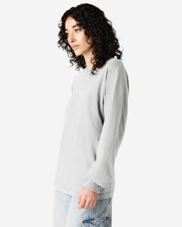 A grey long sleeve t-shirt with a relaxed fit, featuring a logo on the front. The model has curly hair.