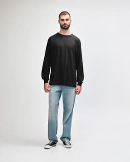 A long sleeve t-shirt in dark grey worn by a model, paired with black trousers and sneakers.