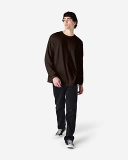 A man wearing a brown long sleeve T-shirt and black jeans, standing against a plain background.