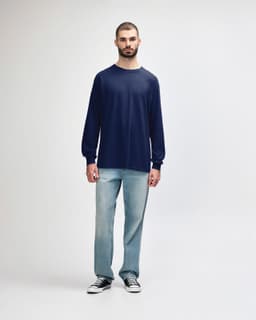 A man wearing a navy long sleeve t-shirt paired with black trousers and sneakers, with a logo visible.