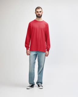 A male model wears a red long-sleeve t-shirt paired with black jeans and sneakers. The shirt features a logo.