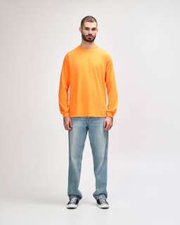An orange long sleeve t-shirt worn by a standing male model, paired with black pants and sneakers.