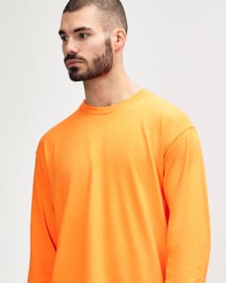 An orange long sleeve T-shirt on a model, featuring a simple design and a logo on the shirt.